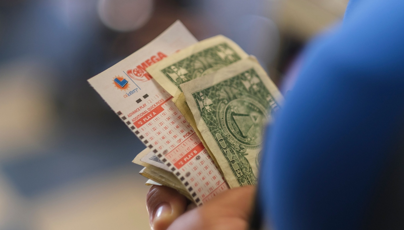 The hand of a California Lottery player holding a Mega Millions play slip while waiting in line to play.