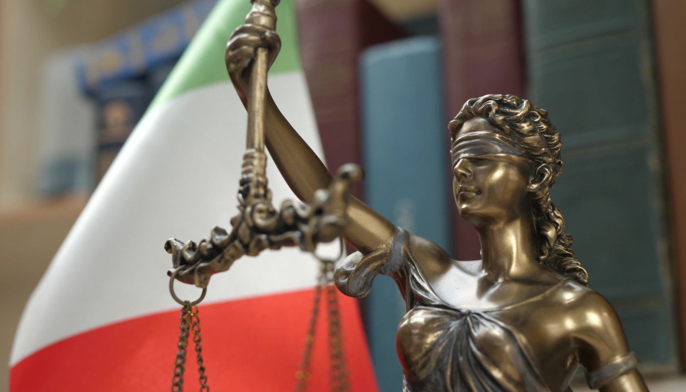 A statue of Lady Justice with books and the Italian flag on the background.