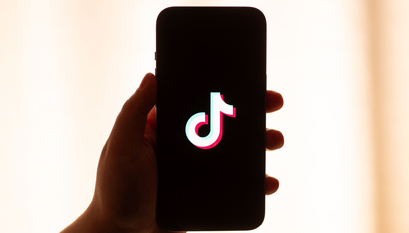 A hand holding a phone with the TikTok logo on screen.