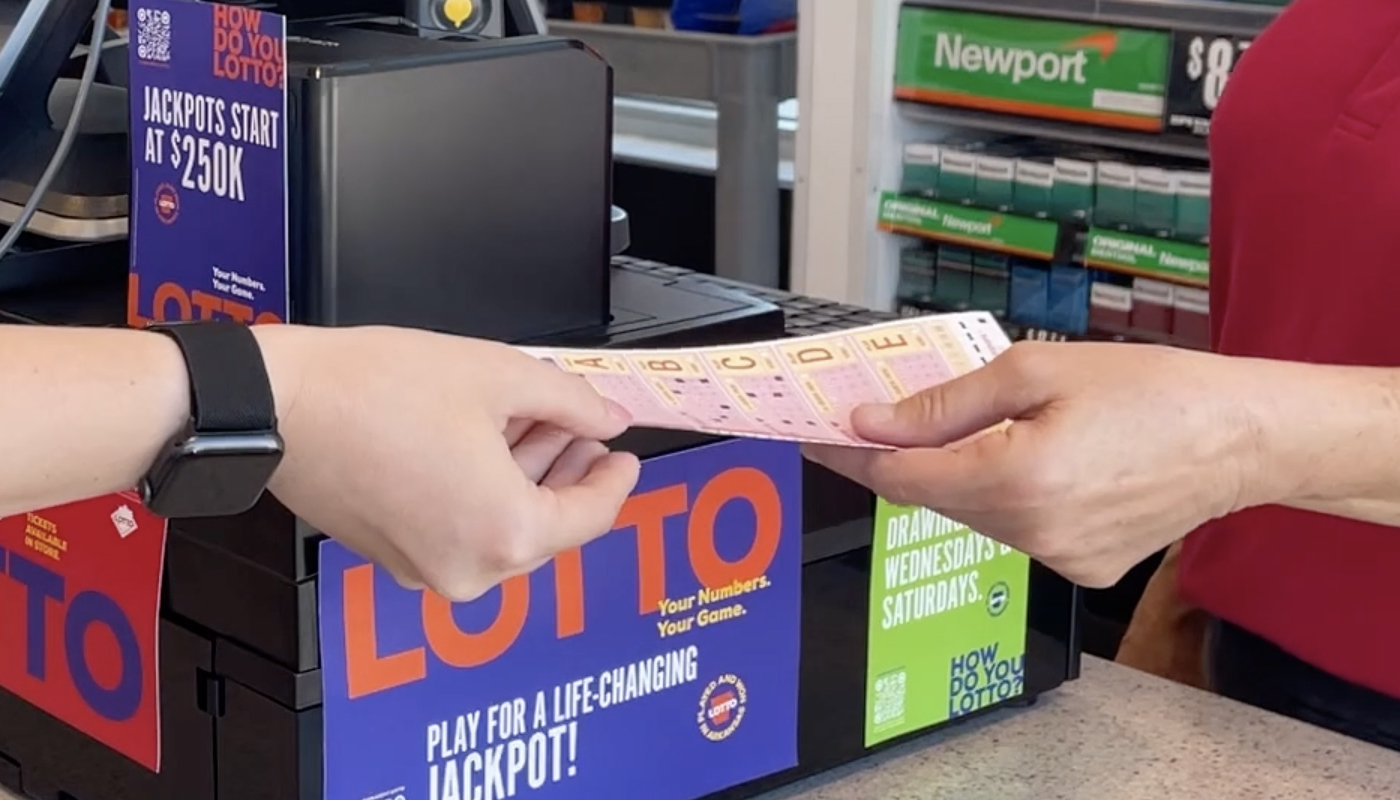 A person handing over a lottery play slip to a lottery retailer.