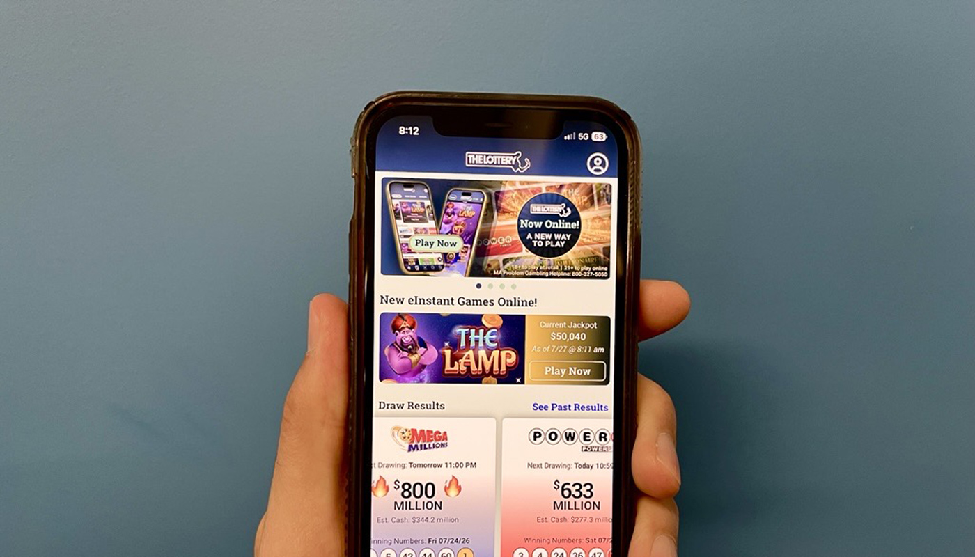 A hand holding a phone with the Massachusetts State Lottery website on the screen.