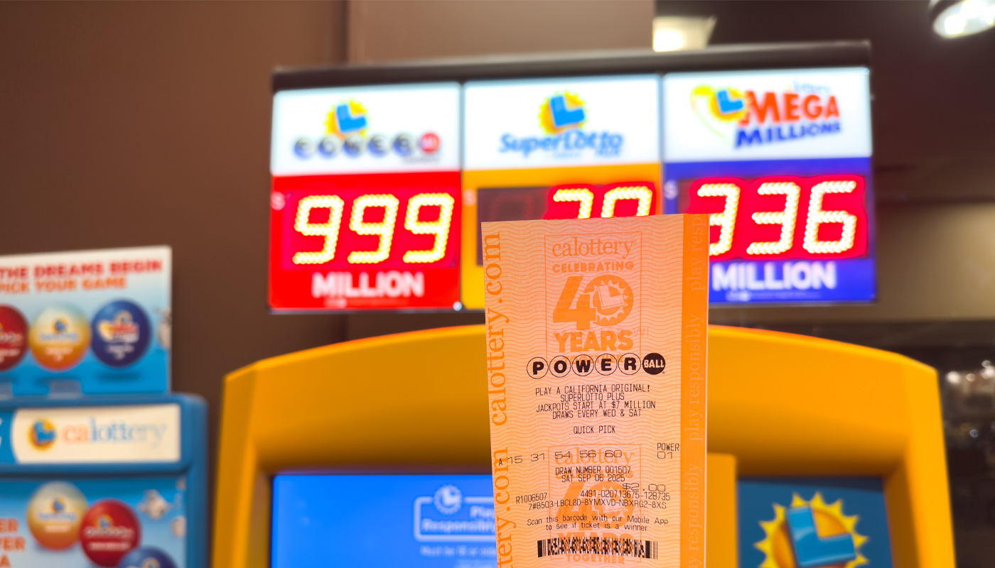 A hand holding a California Lottery Powerball ticket over a LED display showcasing the jackpot.