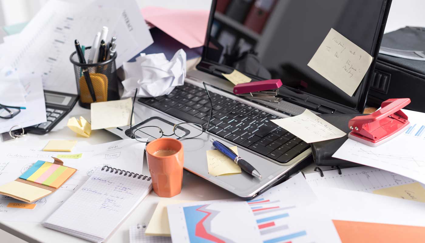 Cluttered desk with a laptop, papers, stationery, and sticky notes.