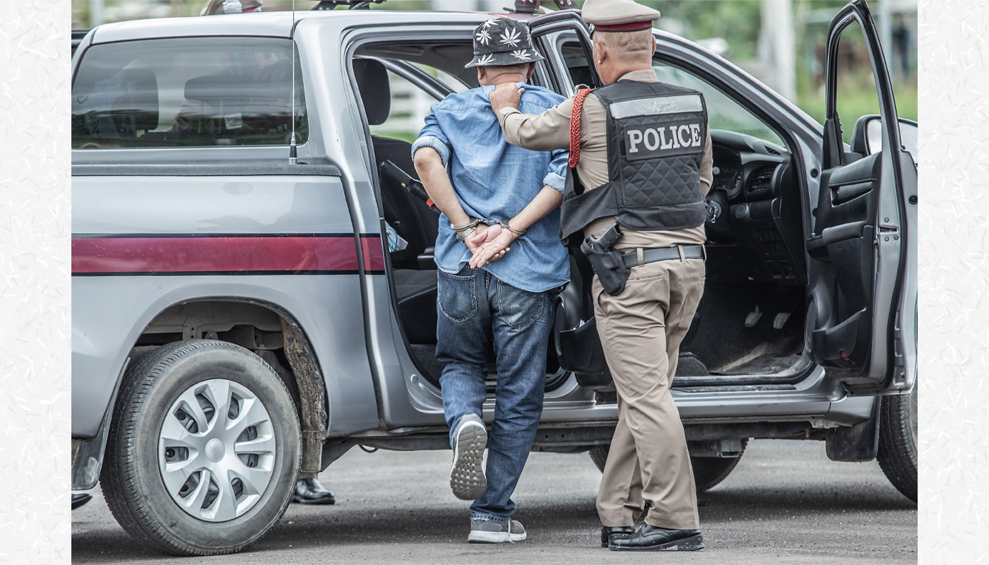 A police officer helps a person in handcuffs into the back of a police car.